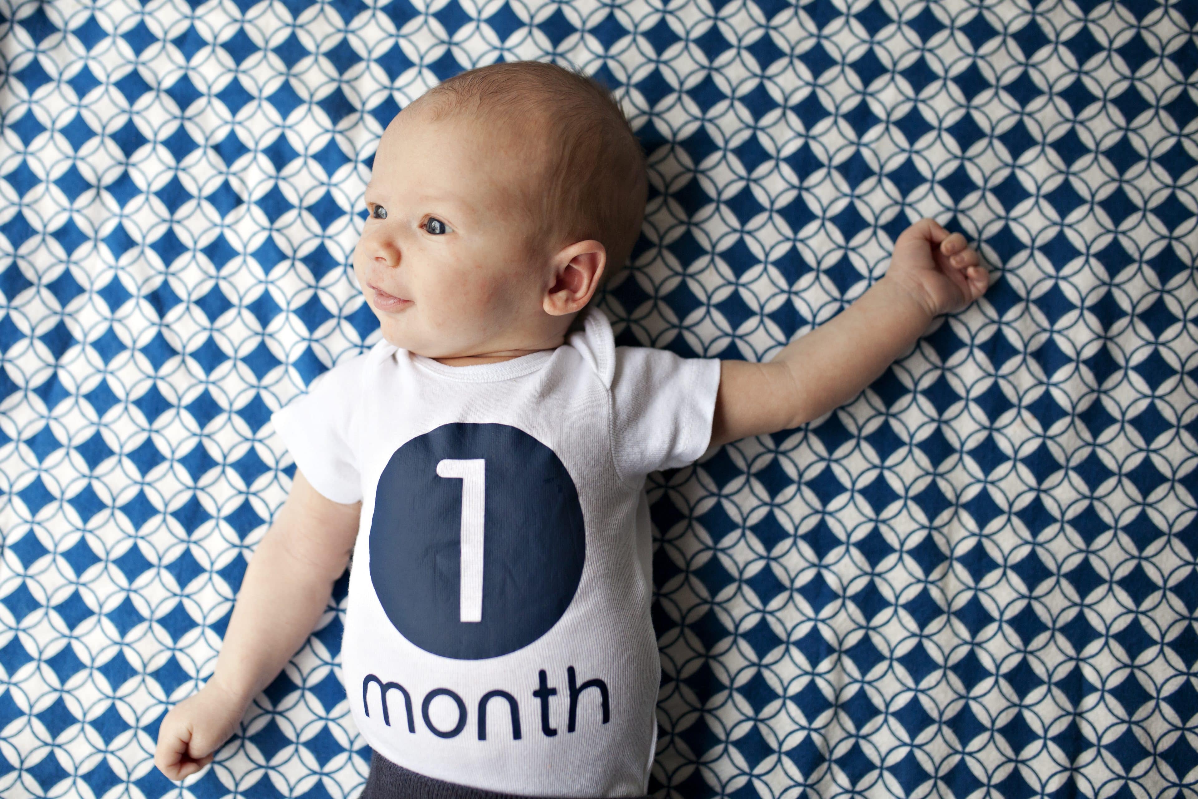 baby boy wearing a one month old shirt lying on a AWP9D6J scaled نمو الطفل الرضيع...ما بين الإرهاق والسعادة! مجلة نقطة العلمية