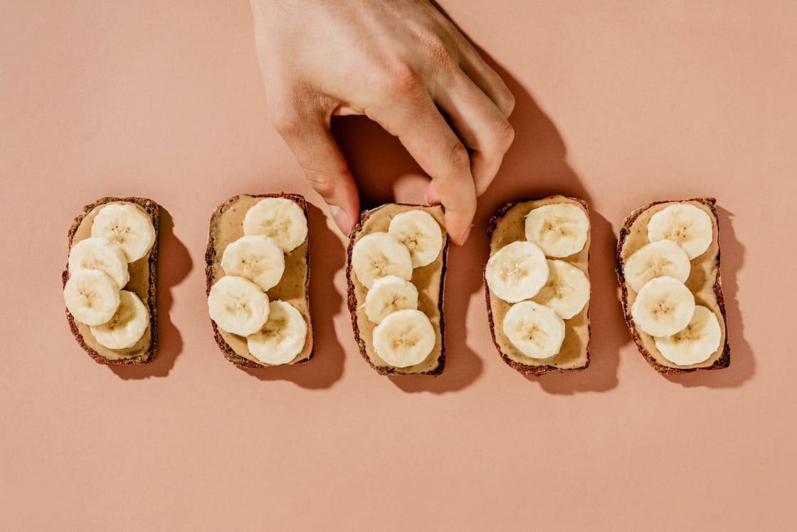 hand reaching for peanut butter banana toasts on pink seamless كيف نميز بين الهوس والأكل الحدسي؟ مجلة نقطة العلمية