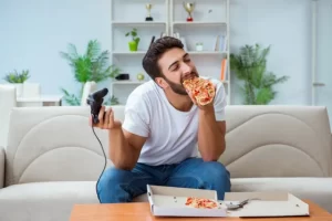 man playing video games eating pizza lazy unhealthy هذا هو السبب الأساسي الأول لمرض السكري! مجلة نقطة العلمية